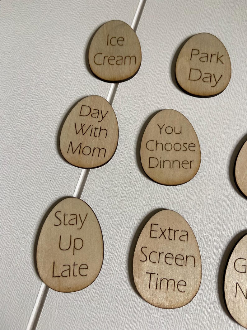 Op de afbeelding: Houten, eivormige tokens met verschillende activiteiten erop geschreven, waaronder "Ijs", "Dagje uit in het park", "Dag met mama", "Jij kiest het diner", "Laat opblijven", "Extra schermtijd" en "Spelletjesavond".