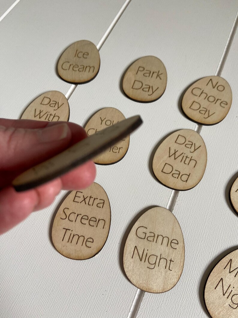 Op de afbeelding: Houten, eivormige tokens met verschillende activiteiten erop geschreven, zoals "IJs", "Dagje uit", "Geen klusjesdag", "Dag met papa", "Extra schermtijd", "Spelletjesavond".