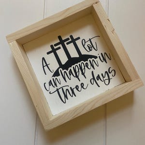 Puede incluir: Un letrero de madera con fondo blanco y letras negras. El letrero dice "Mucho puede pasar en tres d&iacute;as" con tres cruces detr&aacute;s del texto.