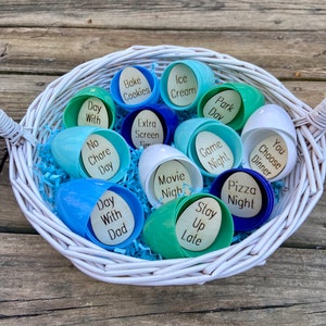 May include: A white wicker basket filled with blue and green plastic Easter eggs. Each egg contains a different activity or treat, such as "Bake Cookies", "Ice Cream", "Park Day", "Movie Night", "Pizza Night", "Stay Up Late", "Day With Dad", "No Chore Day", "Game Night", "You Choose Dinner", and "Day With Dad".