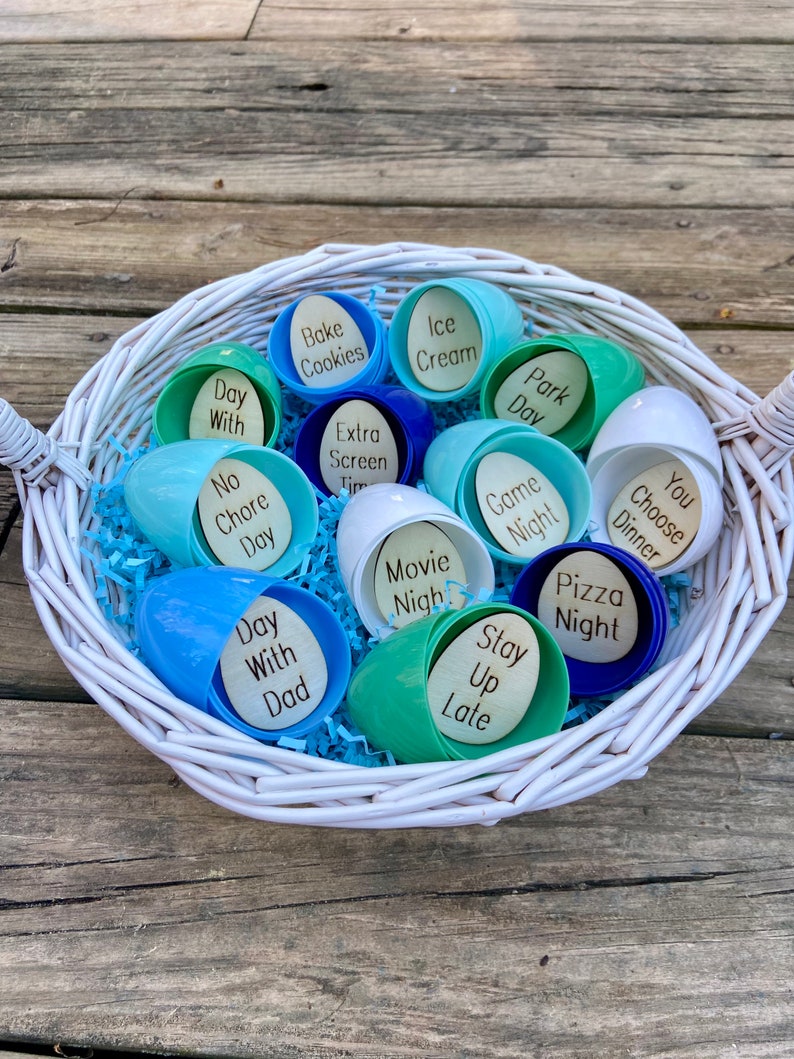 Op de afbeelding: Een witte rieten mand gevuld met blauwe en groene plastic paaseieren. Elk ei bevat een andere activiteit of traktatie, zoals "Bake Cookies", "Ice Cream", "Park Day", "Movie Night", "Pizza Night", "Stay Up Late", "Day With Dad", "No Chore Day", "Game Night", "You Choose Dinner" en "Day With Dad".