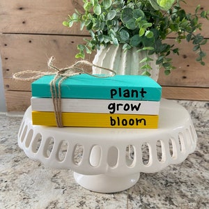May include: Three stacked wooden blocks painted in turquoise, yellow, and white with the words "plant", "grow", and "bloom" written in black.