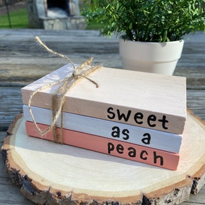 May include: Three stacked wooden blocks painted in shades of pink and white. The top block reads "sweet as a peach" in black lettering.