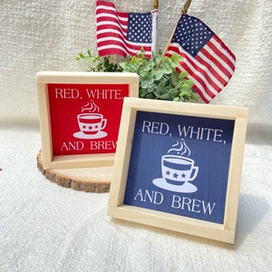 Pu&ograve; includere: Due cartelli in legno con il testo "Red, White, and Brew" e un'immagine di una tazza di caff&egrave;. I cartelli sono dipinti di rosso e blu e hanno una cornice in legno.