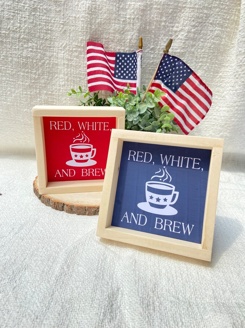 Pu&ograve; includere: Due cartelli in legno con il testo "Red, White, and Brew" e un'immagine di una tazza di caff&egrave;. I cartelli sono dipinti di rosso e blu e hanno una cornice in legno.
