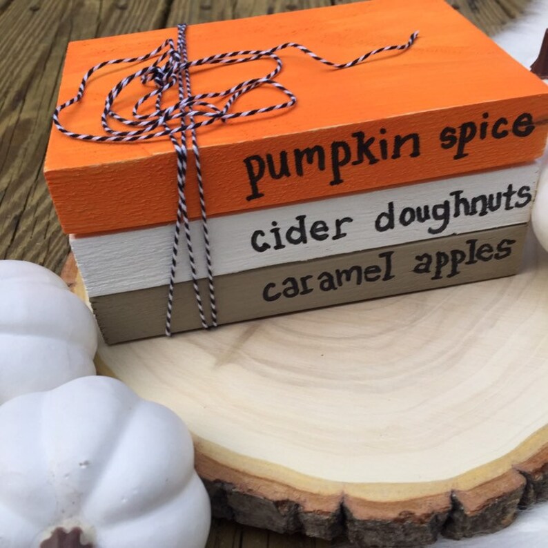 K&ouml;nnte beinhalten: Ein Stapel aus drei Holzbl&ouml;cken, die in Orange, Wei&szlig; und Braun mit schwarzer Schrift bemalt sind. Der obere Block lautet "pumpkin spice", der mittlere Block lautet "cider doughnuts" und der untere Block lautet "caramel apples".