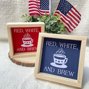Pu&ograve; includere: Due cartelli in legno con il testo "Red, White, and Brew" e una grafica di una tazza di caff&egrave;. I cartelli sono dipinti di rosso e blu e hanno una cornice in legno.