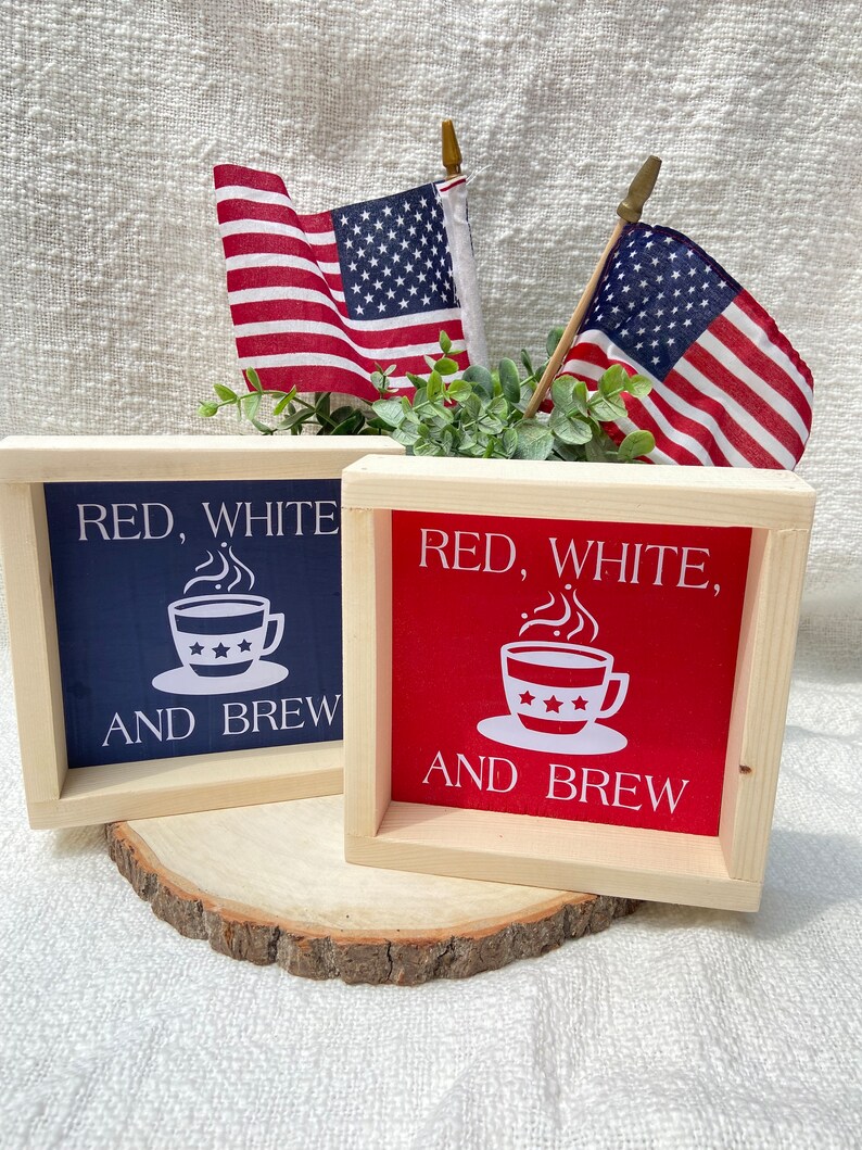 Pu&ograve; includere: Due cartelli in legno con il testo "Red, White, and Brew" e un'immagine di una tazza di caff&egrave;. I cartelli sono dipinti in rosso, bianco e blu. I cartelli sono appoggiati su una fetta di legno.