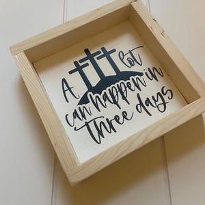 Puede incluir: Un letrero de madera con fondo blanco y letras negras. El letrero dice "Mucho puede pasar en tres d&iacute;as". Hay tres cruces negras detr&aacute;s del texto.