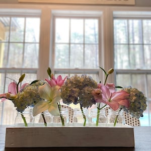 May include: A white wooden box with a sign that reads "FRESH FLOWERS" above it. The box holds seven glass jars filled with pink, white, and blue flowers.
