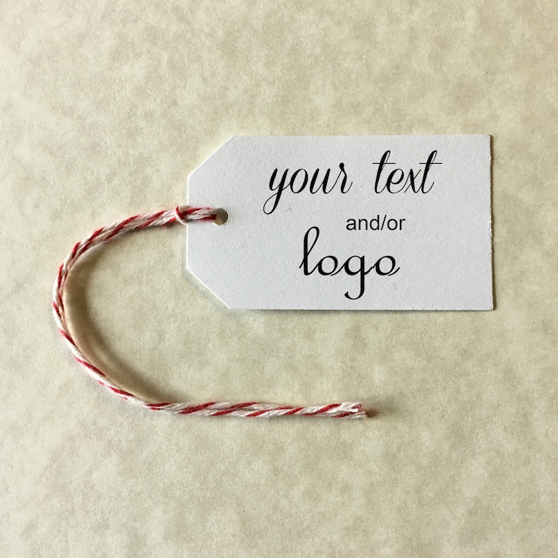 Puede incluir: Etiqueta de regalo blanca con una cuerda de yute roja y blanca. La etiqueta tiene el texto "your text and/or logo" impreso en ella.