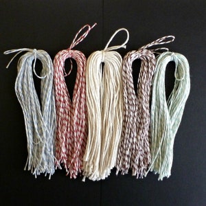 May include: Five spools of twine, each with a different colour pattern. The spools are arranged in a row from left to right: light blue and white, red and white, white, brown and white, and light green and white.