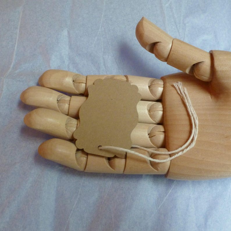 May include: A wooden hand model holding a brown paper gift tag with a string attached.