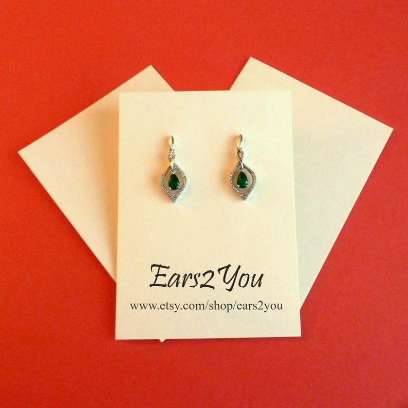 May include: A pair of silver dangle earrings with a pear-shaped green gemstone set in a silver frame. The earrings are on a white card with the text "Ears2You" and the website address "www.etsy.com/shop/ears2you".