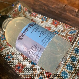 May include: A clear glass bottle with a blue and white label that reads "VIRGIN'S" and includes text about the product's use and ingredients. The bottle is sitting on a patterned surface.