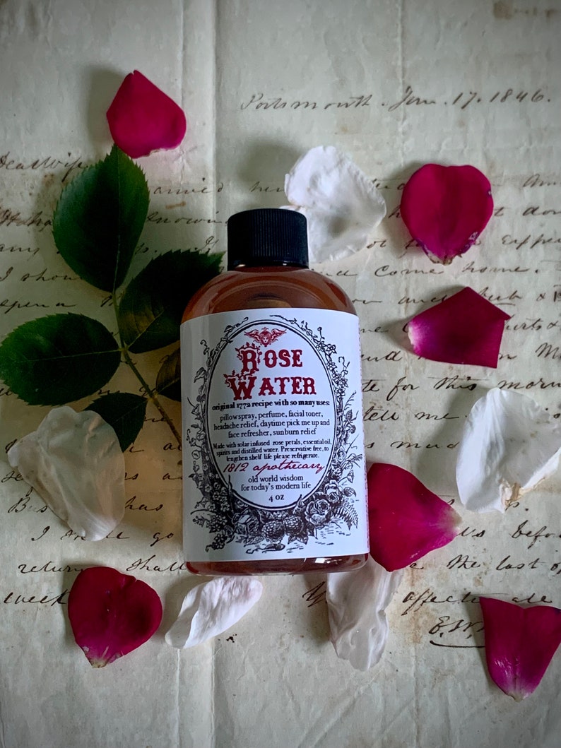 Op de afbeelding: Een doorzichtige glazen fles met een bruine vloeistof erin. De fles is gelabeld met "ROSE WATER" en heeft een vintage ontwerp met een bloemenmotief. De fles staat op een stuk papier met handgeschreven tekst.