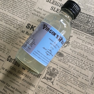 May include: A clear glass bottle with a blue label that reads "Virgin's Milk" and "renders the skin clear and brilliant". The bottle is sitting on a newspaper with text about a coal company and a lodge meeting.