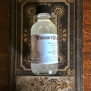May include: A clear glass bottle with a black cap and a white label that reads "VIRGIN'S MILK renders the skin soft and beautiful 1779 1812 apothecary Ladies use it naturally for a clear complexion, for which purpose it is better, or indeed to make it whiter."