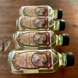 May include: Four small glass bottles with black caps and labels that say "Milk of Frankincense" in a vintage style font. The labels feature a woman in a white dress and a floral design.