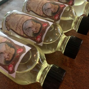 May include: Four clear glass bottles with black caps filled with a light yellow liquid. Each bottle has a label with a vintage design featuring a woman and roses. The label text reads "Pure Oil of Frankincense".