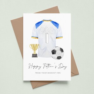 May include: A Father's Day card featuring a watercolor illustration of a soccer jersey with the word "DAD" and the number "1". A soccer ball and a trophy are also depicted. The card reads "Happy Father's Day FROM YOUR BIGGEST FAN".