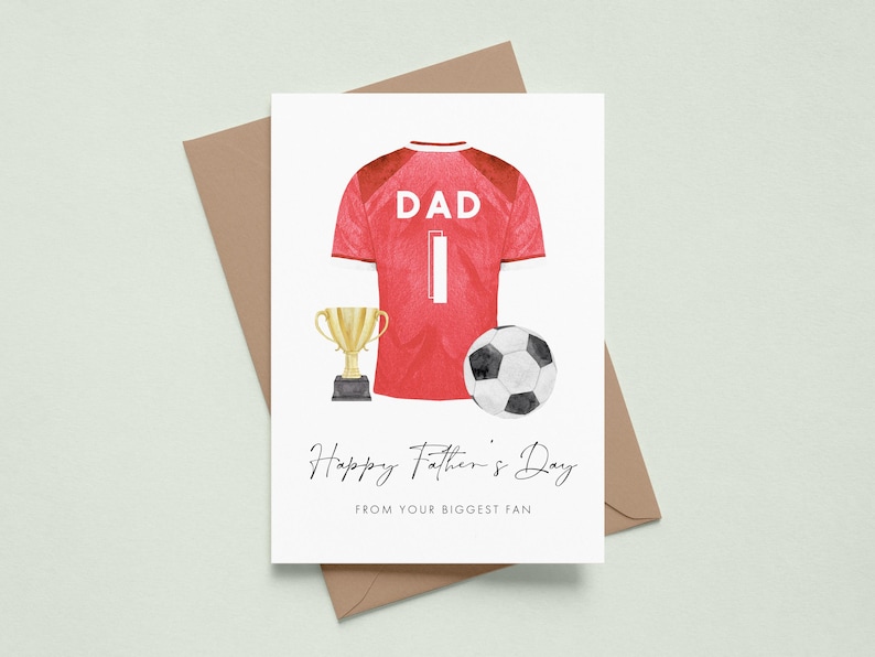 May include: Father's Day greeting card featuring a red soccer jersey with the word "DAD" and the number 1. A gold trophy and a soccer ball are also depicted. The card includes the text "Happy Father's Day FROM YOUR BIGGEST FAN."
