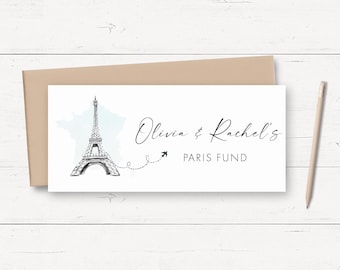 May include: A rectangular white card featuring a black ink sketch of the Eiffel Tower, a light blue map outline of France, and a dashed flight path leading to a small airplane. The text reads Olivia & Rachel's PARIS FUND.