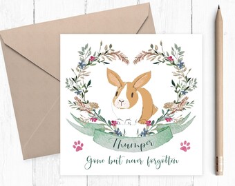 May include: A square greeting card featuring a brown and white rabbit illustration centered within a floral wreath. A green banner below the rabbit reads Thumper, with the text Gone but never forgotten below. Two pink paw prints flank the banner.