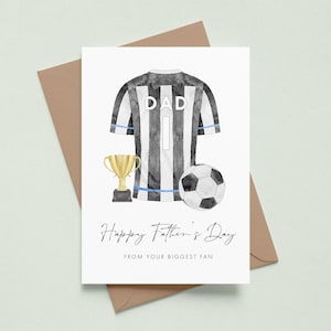 May include: A Father's Day card with a watercolor illustration. The card features a black and white striped soccer jersey with the word "DAD" and the number 1. A gold trophy and soccer ball are also depicted. The text reads "Happy Father's Day from your biggest fan."