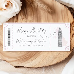 May include: A rectangular paper ticket with a light pink border and small heart icons in the corners. It features a barcode, a sketch of Big Ben, a dotted flight path, and the text: Happy Birthday JACOB We're going to London! PACK YOUR BAGS, LOVE SARAH X.