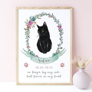 May include: A framed print featuring a watercolor illustration of a black cat centered within a floral wreath. Below the cat, a green ribbon displays the name Salem, the dates 2010-2018, two paw prints, and the text no longer by my side, but forever in my heart.