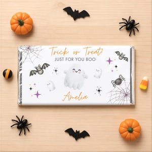 May include: A rectangular candy bar wrapper featuring the text Trick or Treat! JUST FOR YOU BOO and the name Amelia. The design includes illustrations of white ghosts, gray bats, black spiders, spider webs, and purple and black star accents.