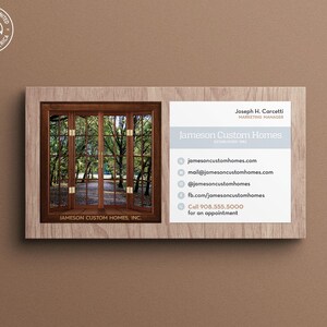 May include: A business card for Jameson Custom Homes, featuring a photo of a wooden window with a view of a wooded area. The card includes the company's name, website, email address, social media handles, and phone number.