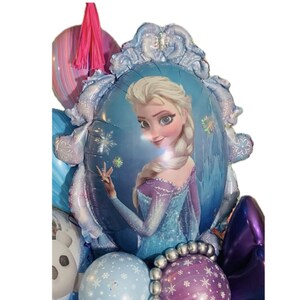May include: A collection of colorful balloons, including a large, oval-shaped balloon featuring a portrait of Elsa from the movie Frozen. The balloons are in shades of blue, purple, and pink, with snowflake and floral patterns.