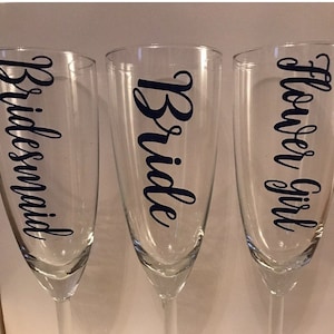 May include: Three champagne flutes with black vinyl lettering. The flutes are labeled "Bride", "Bridesmaid", and "Flower Girl".