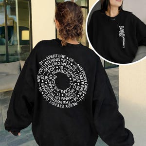 以下が含まれることがあります： 黒い持ち手と「But First, Coffee」の文字が黒い手書き風フォントで書かれた白いセラミックマグ。マグカップは白い表面に置かれています。