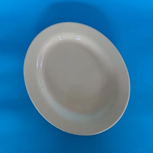May include: An oval, cream-coloured serving platter against a bright blue background. The platter has a smooth, glossy finish and a slightly raised edge. The shape is ideal for serving appetizers or main courses.