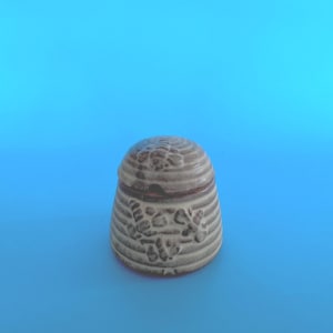 May include: A small, ceramic jar with a lid. The jar is light grey with horizontal ridges and floral designs. The lid is rounded with a similar pattern. The jar is set against a bright blue background.