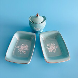 May include: A set of three vintage ceramic dishes in a light blue colour with a white floral design. The set includes two rectangular dishes and a lidded sugar bowl.