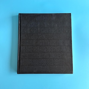May include: A black hardback book with a grid-like embossed pattern on the front cover. The text "THE 21ST CENTURY" is integrated into the design, featuring a series of square tiles with various geometric and abstract patterns surrounding the lettering.