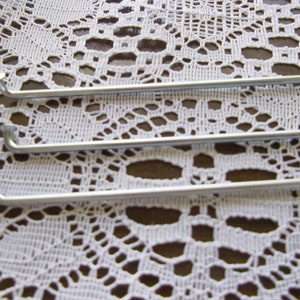 May include: Three silver bicycle spokes, lying on a white lace tablecloth.