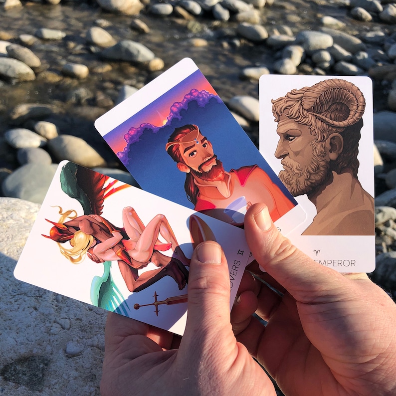 May include: Three tarot cards, one with a depiction of a winged figure, another with a man with a crown and a third with a man with a ram's head. The cards are labelled "Lovers II", "Emperor" and "Aries".