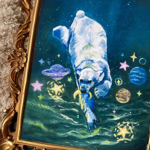 May include: A painting of a polar bear swimming in a dark blue sea with stars and planets in the background. The bear is holding a crescent moon in its mouth.