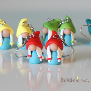 May include: A set of colorful gnome earrings made of polymer clay. The gnomes are wearing blue shirts, red, yellow, and green hats, and have white beards. The earrings are attached to silver hooks.