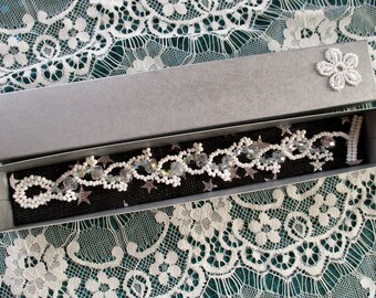 Puede incluir: Un brazalete blanco de cuentas con detalles de cristal y abalorios en forma de estrella en una caja de regalo gris.