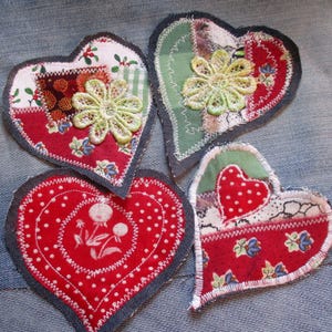 Könnte beinhalten: Vier rote und grüne Stoffherzen mit weißen Nähten und Spitzendetails. Die Herzen sind auf einen blauen Jeansstoff genäht.