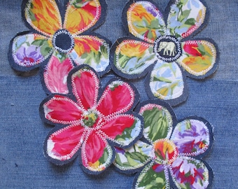 May include: Three fabric flower appliques with denim borders and white zigzag stitching. The flowers feature multi-colored floral patterns in shades of red, yellow, purple, and green. One flower center displays a small white elephant graphic.