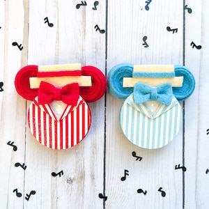 May include: Two decorative felt ornaments. One is red and white striped with a red bow tie, the other is blue and white striped with a blue bow tie. Both have a cream-colored top and are surrounded by black musical notes.