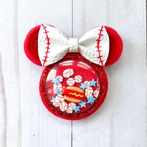 May include: Red felt Minnie Mouse ears with a white bow and a clear plastic dome filled with baseballs, stars, and a hot dog.