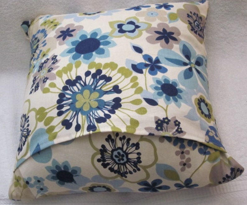 May include: Square decorative pillow with a floral pattern in shades of blue, green, and gray on a cream background. The pillow features a repeating design of stylized flowers.